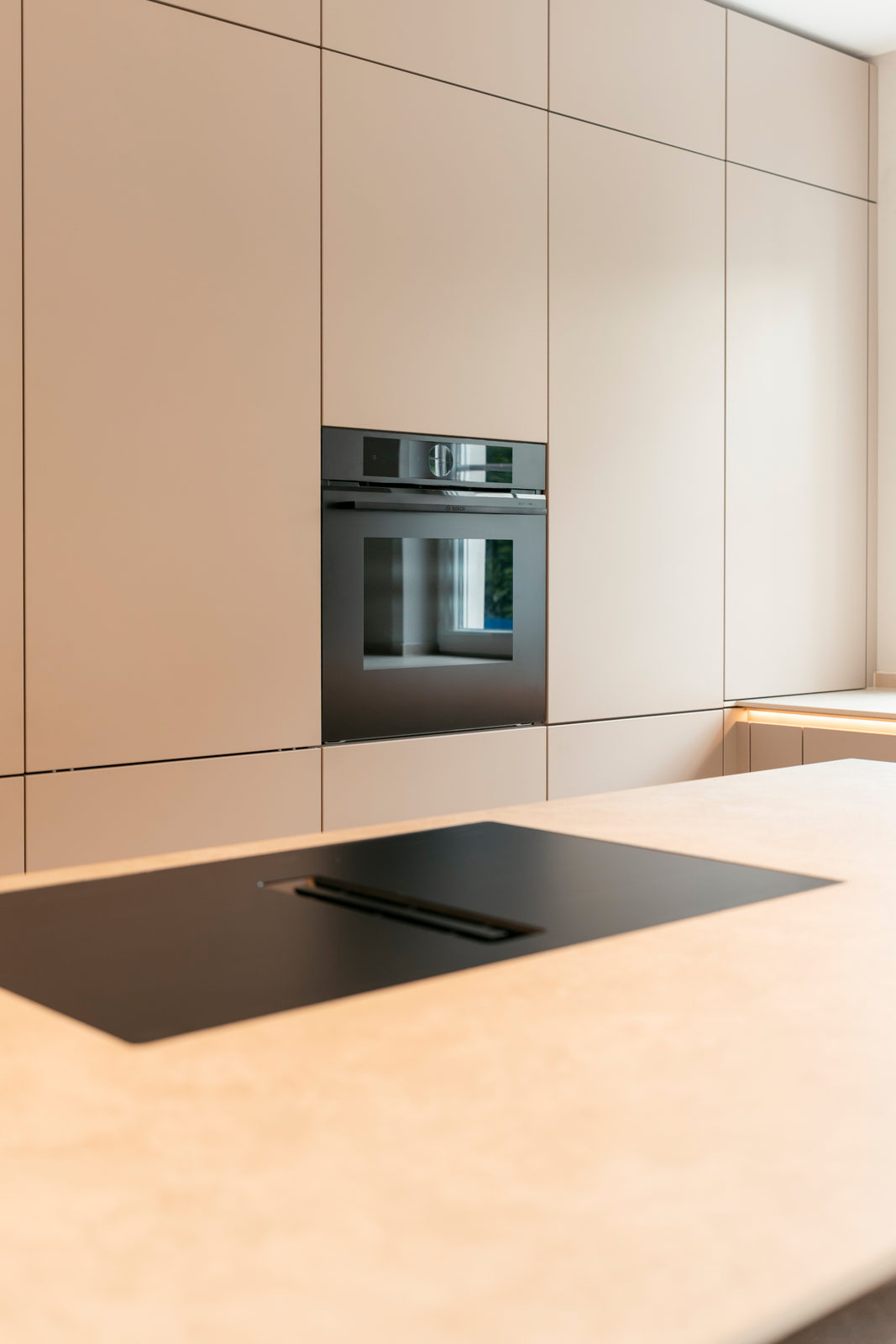 Raumhohe grifflose Schrankwand in Sandbeige mit durchlaufendem Fugenbild und flächenbündig eingebautem Backofen