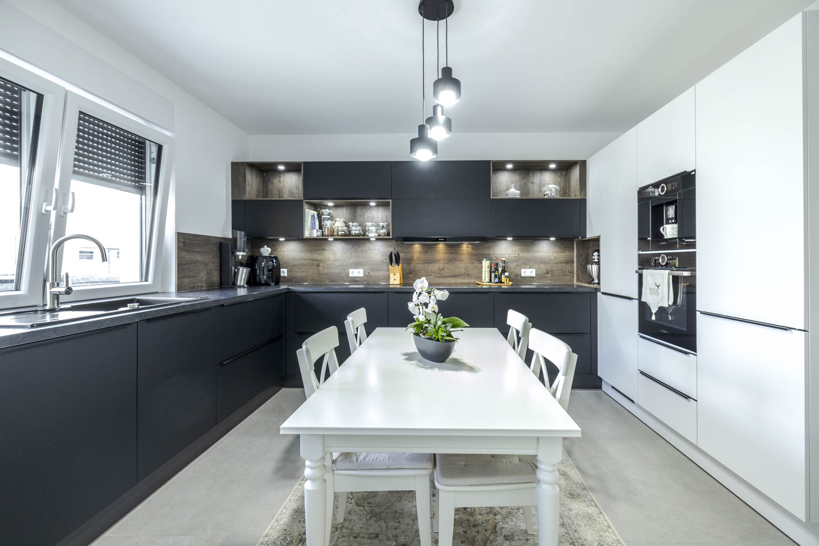Moderne U-Küche mit matt schwarzen „Feel“-Fronten, weißer Schrankwand mit Bosch-Geräten und Nischenrückwand in Eiche Tabak