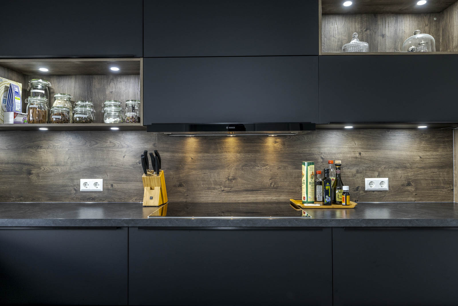 Arbeitsplatte in schwarzer Granitoptik mit Nischenrückwand in Eiche Tabak und beleuchteten Regalnischen
