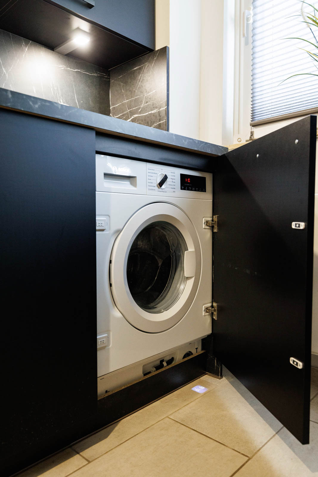 Vollintegrierte Bosch-Waschmaschine hinter der geöffneten schwarzen Lackfront