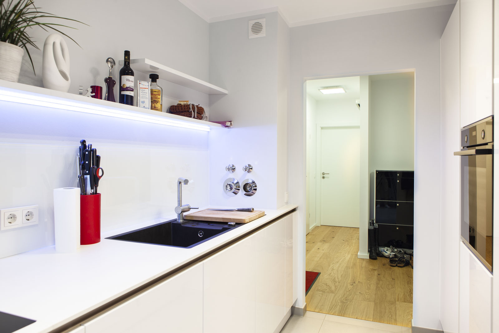 Spülbereich mit schwarzem Becken, Glasnischenverkleidung und LED-beleuchtetem Wandbord