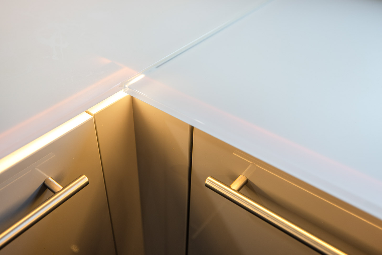 Detail der weißen Glasarbeitsplatte an der L-Ecke mit Stangengriffen und LED-Licht