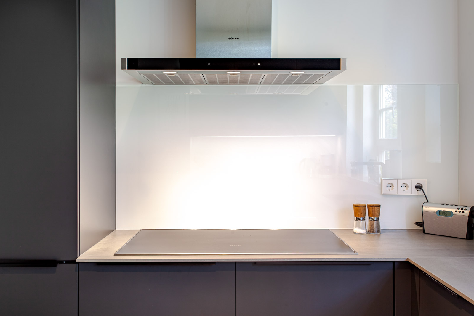 Weiße Glas-Nischenrückwand aus Lacobel Pure White hinter Kochfeld und Edelstahl-Dunstabzug