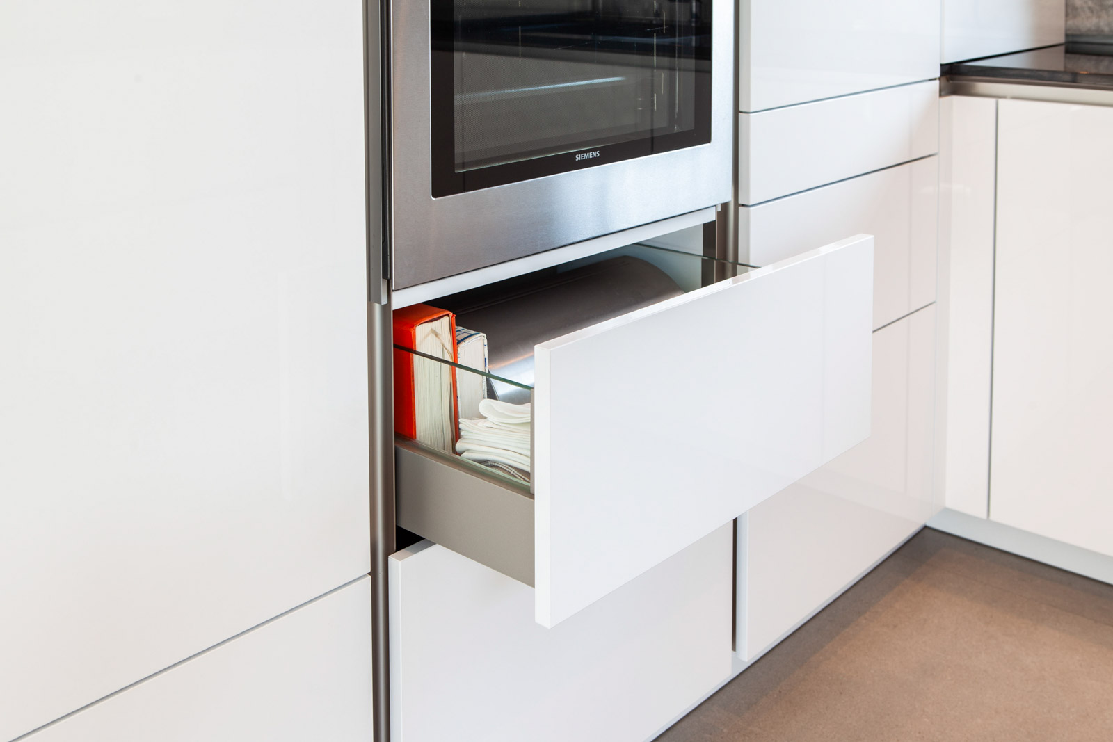 Ausgezogene Schublade mit Glaszargen unter dem Siemens-Backofen im weißen Hochglanz-Hochschrank