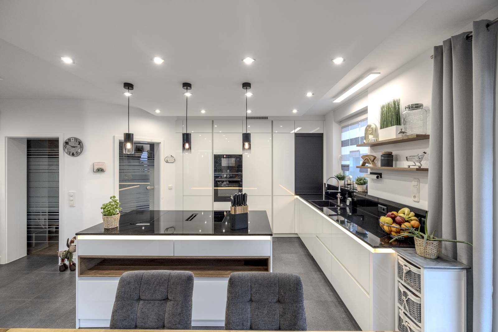 Moderne weiße grifflose Inselküche von Ballerina in Premiumweiß Hochglanz mit schwarzer Naturstein-Arbeitsplatte und integriertem Holzregal