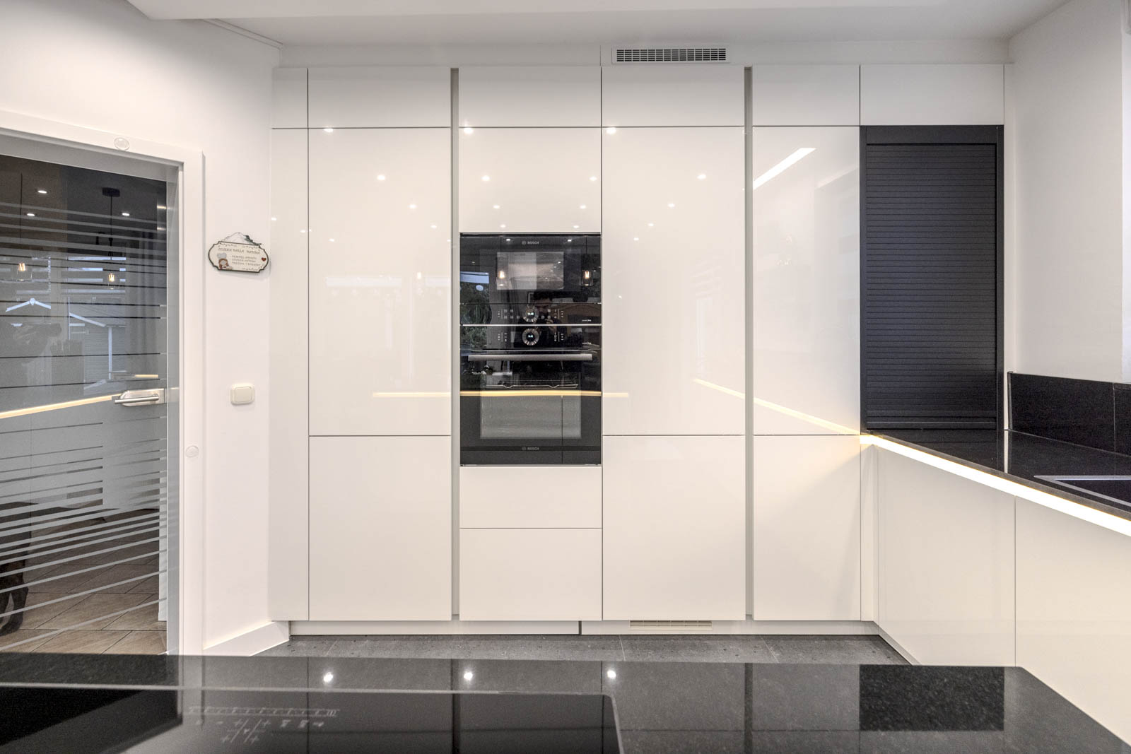 Grifflose Hochschrankwand in Premiumweiß Hochglanz mit eingebauten Bosch-Geräten und schwarzem Jalousieschrank