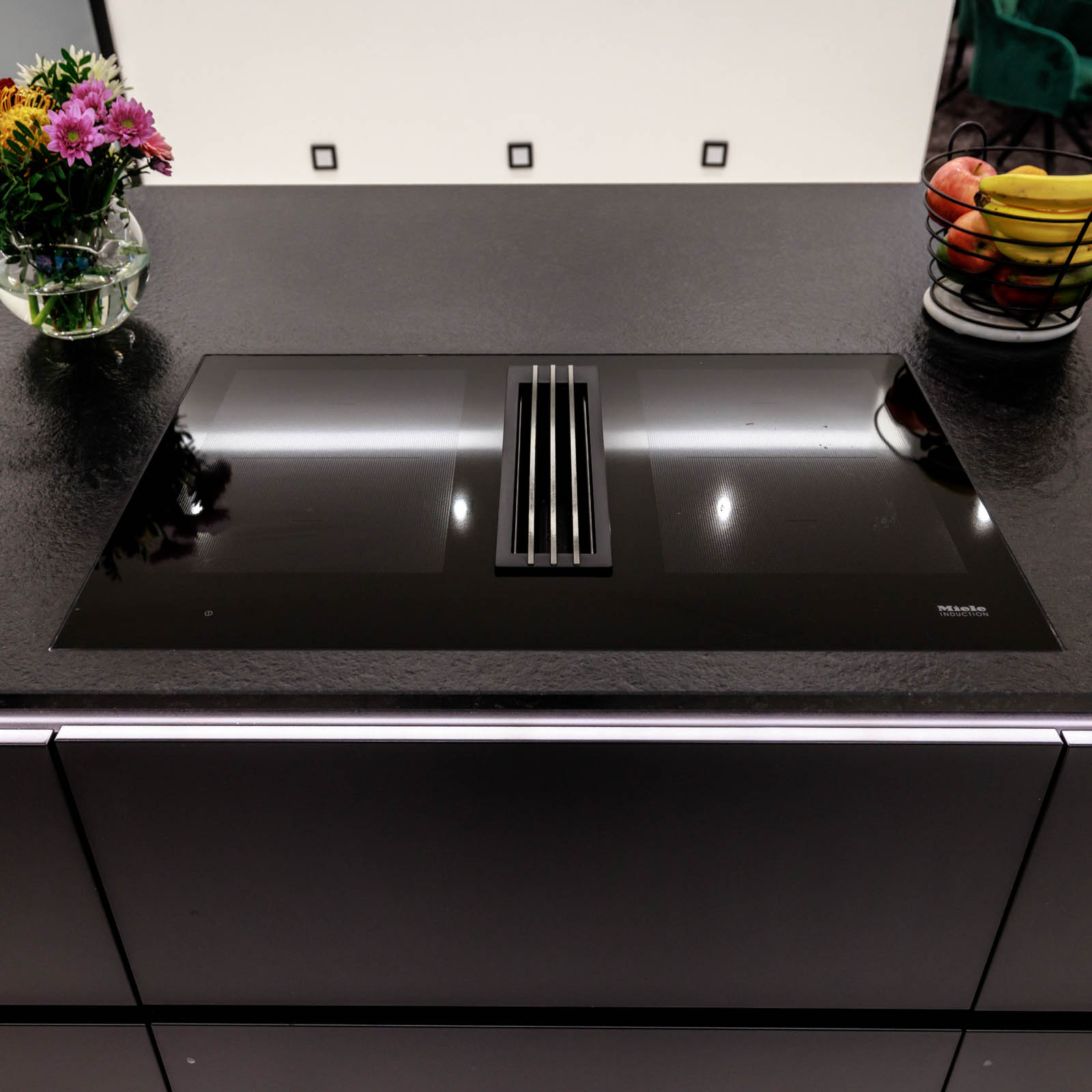 Flächenbündiges Miele-Induktionskochfeld mit Muldenlüfter in der Nero-Assoluto-Arbeitsplatte aus geflammtem und gebürstetem Naturstein