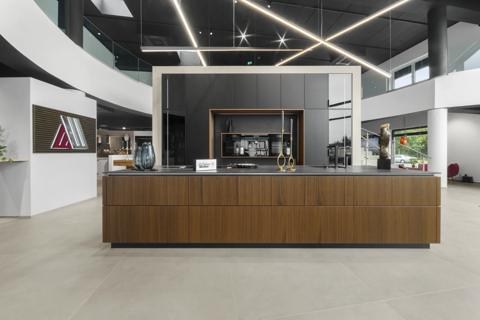 Kücheninsel in Nussbaum mit dunkelgrauer Schrankwand unter den Lichtlinien der Showroom-Decke